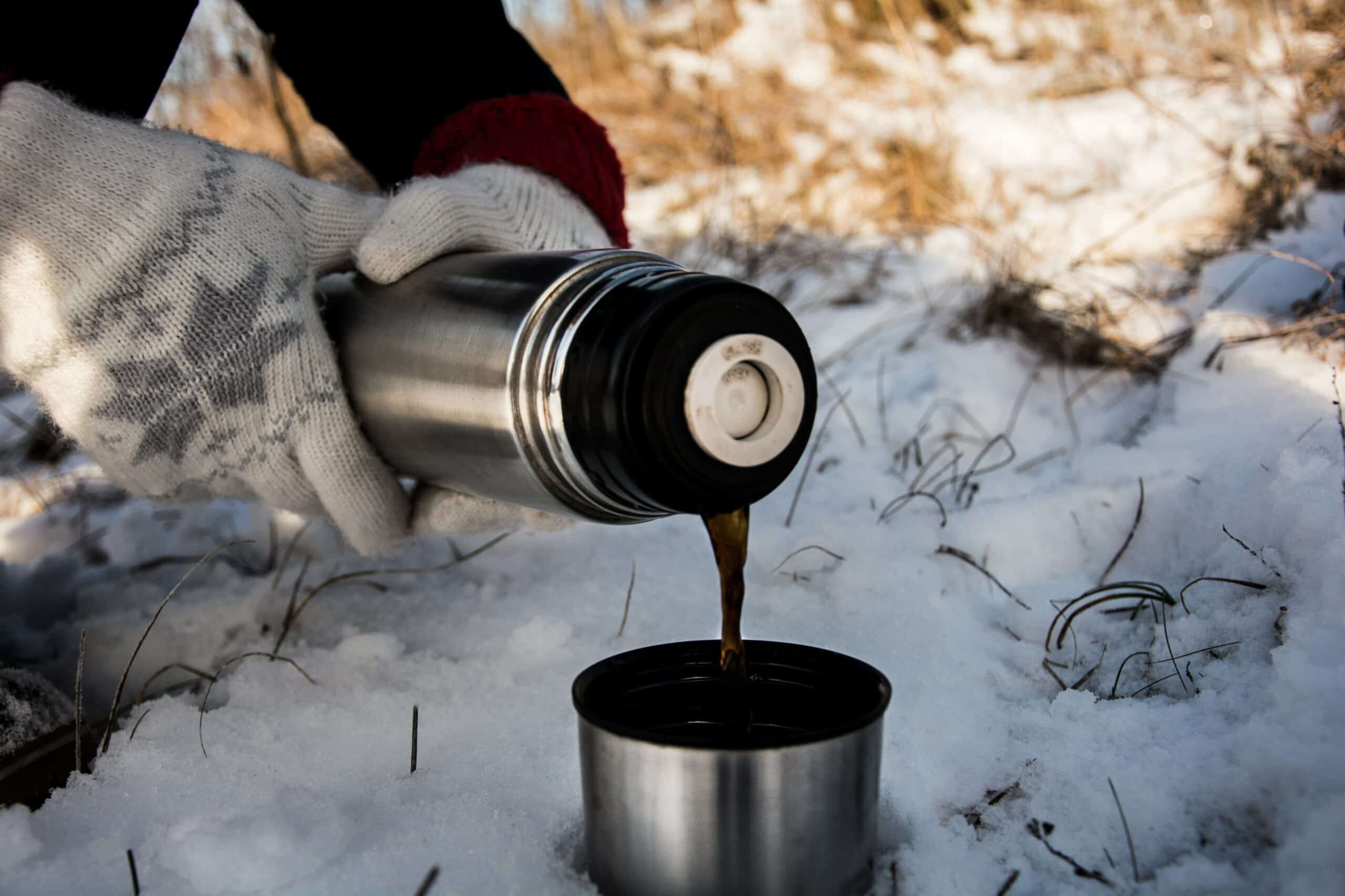 Eine Person schenkt im Winter im Freien Kaffee in einen Becher aus