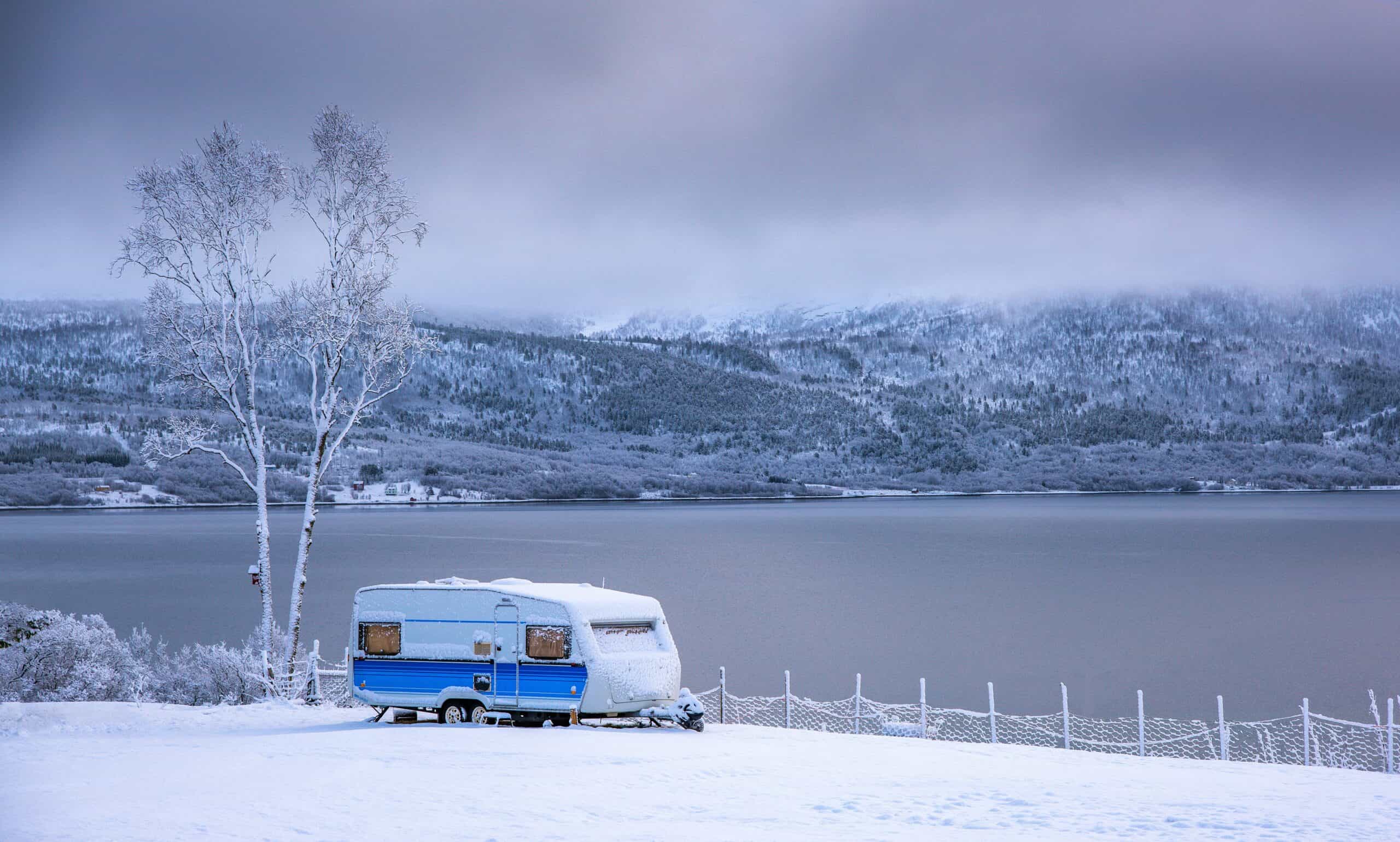 Ein Wohnwagen parkt eingeschneit neben einem See
